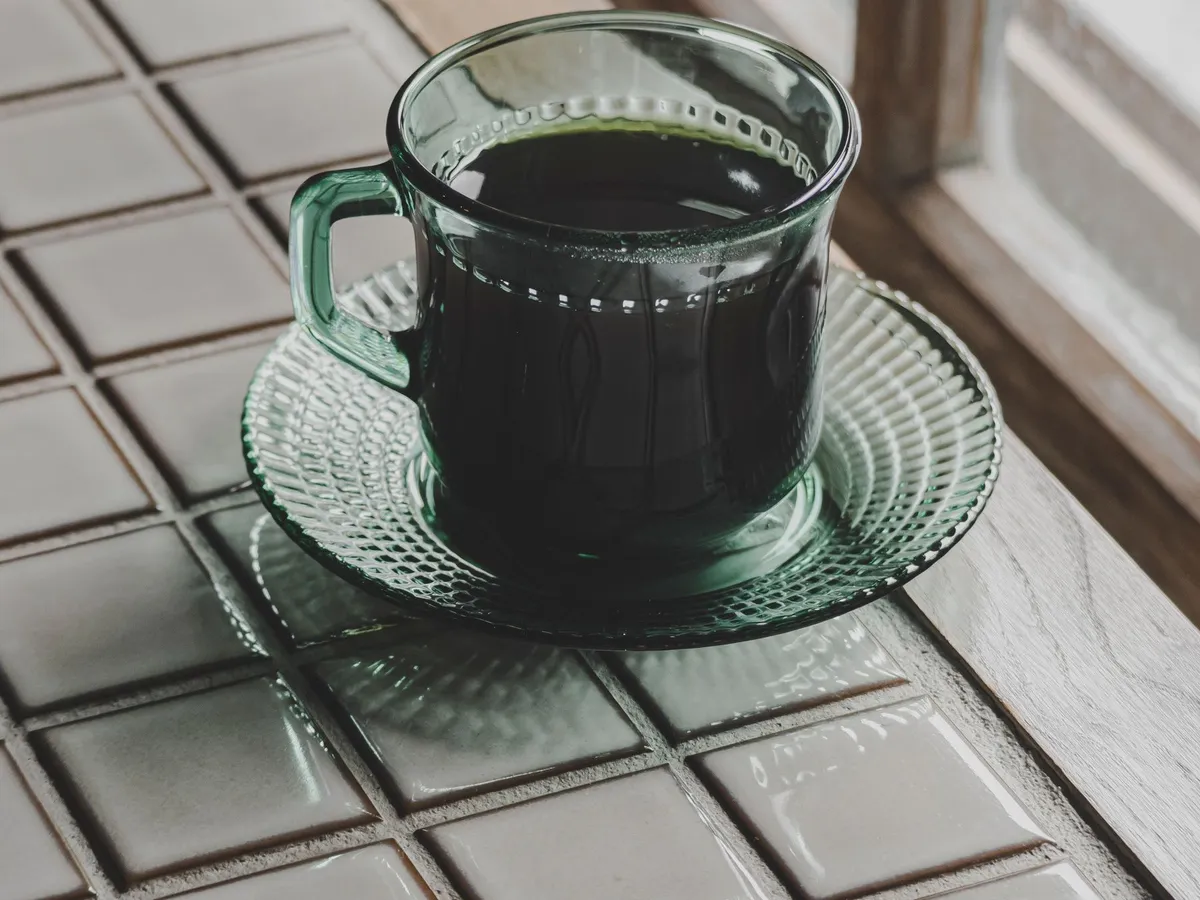 Black coffee in a green glass cup by a window