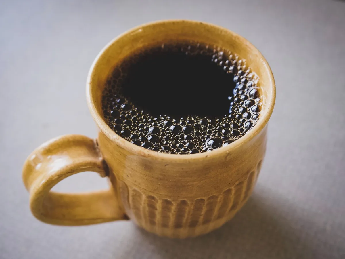 黄色い陶器のマグカップに入った、泡のあるブラックコーヒー