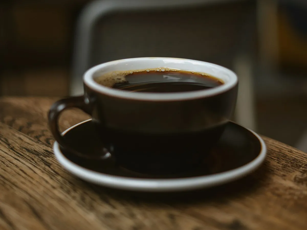 木のテーブルの上の濃い色のカップに入ったブラックコーヒー