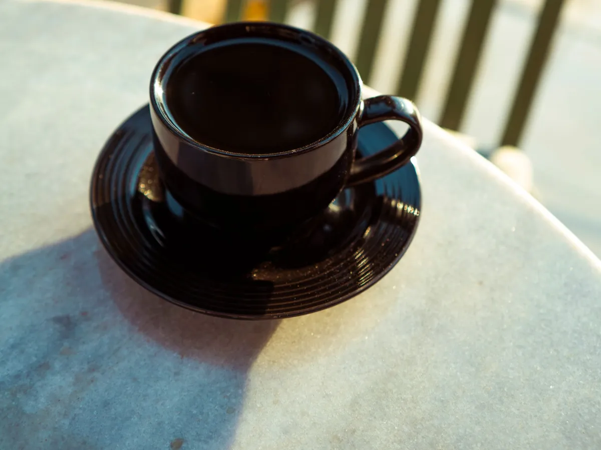 日の当たるテーブルの上の濃い色のカップに入ったブラックコーヒー