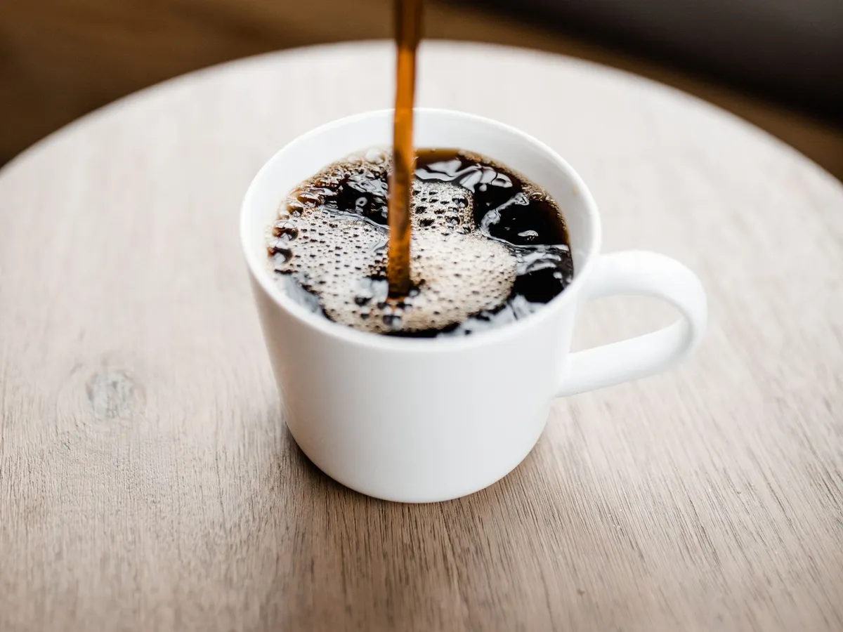 Black coffee being poured into a white mug