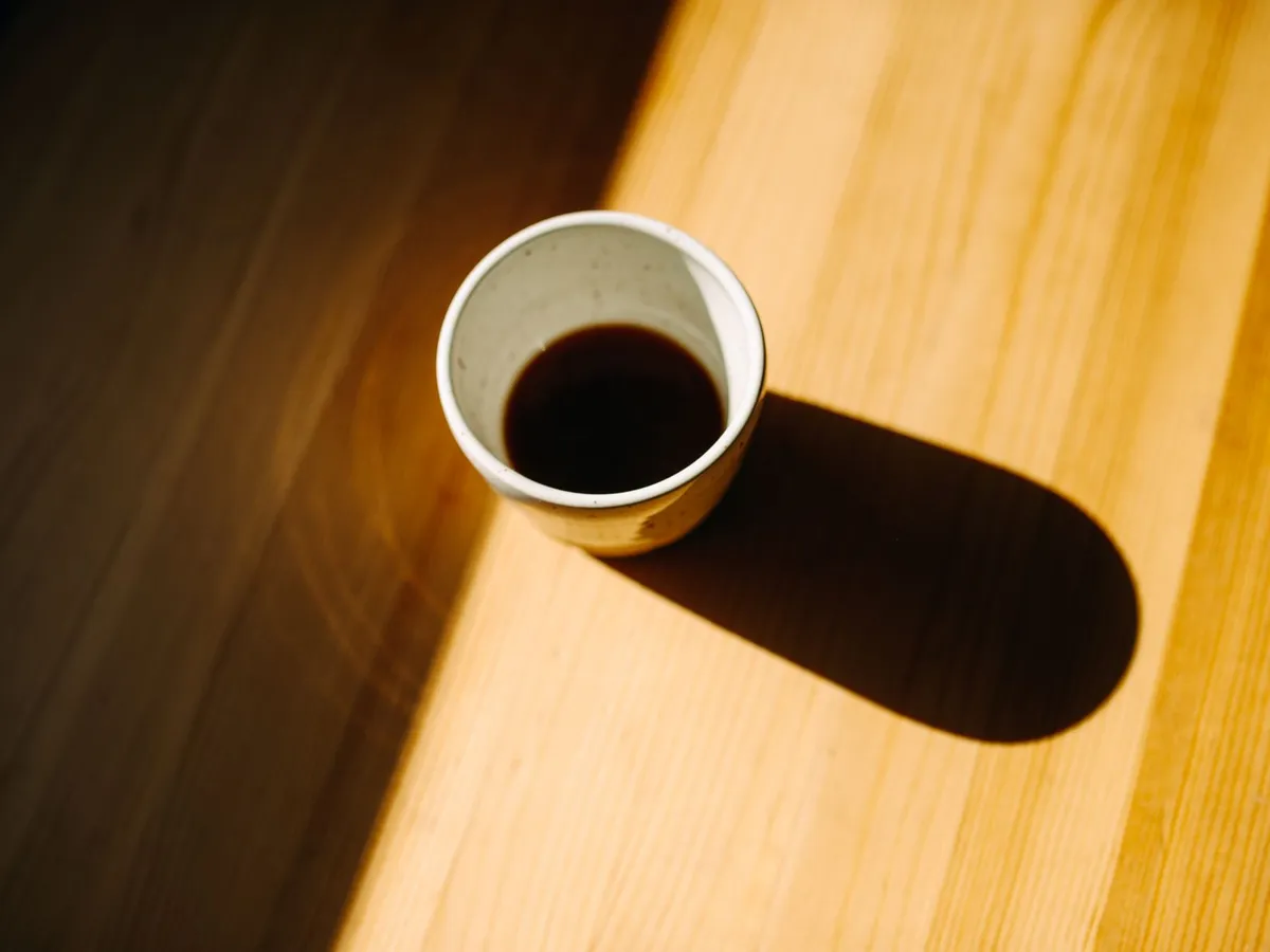 テーブルに影を落とすブラックコーヒー入りのマグカップ